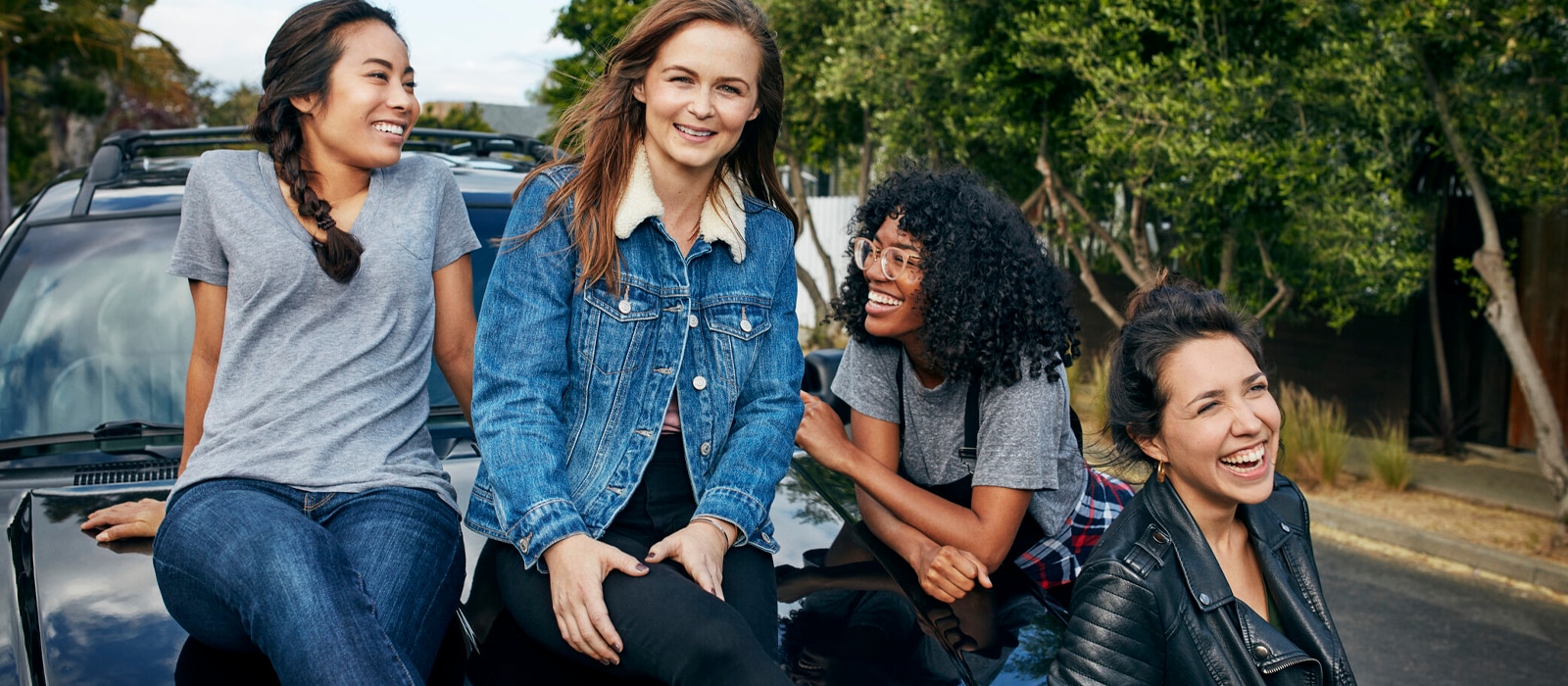 Picture of 4 young women laughing and smiling while sitting on the front of a car
